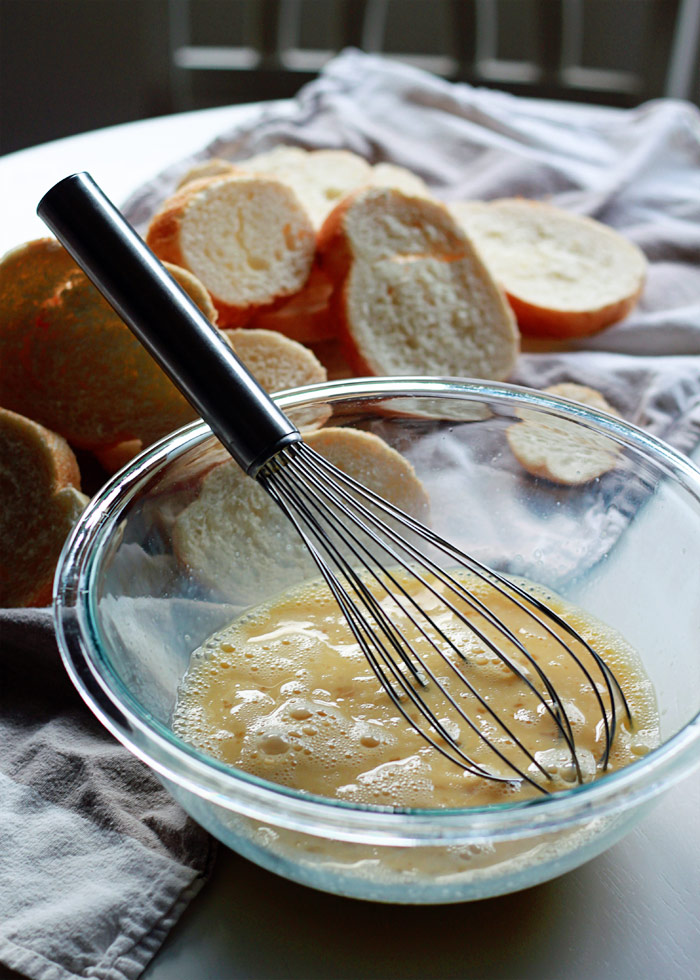 A bowl of French toast batter with a whisk and bread in the background