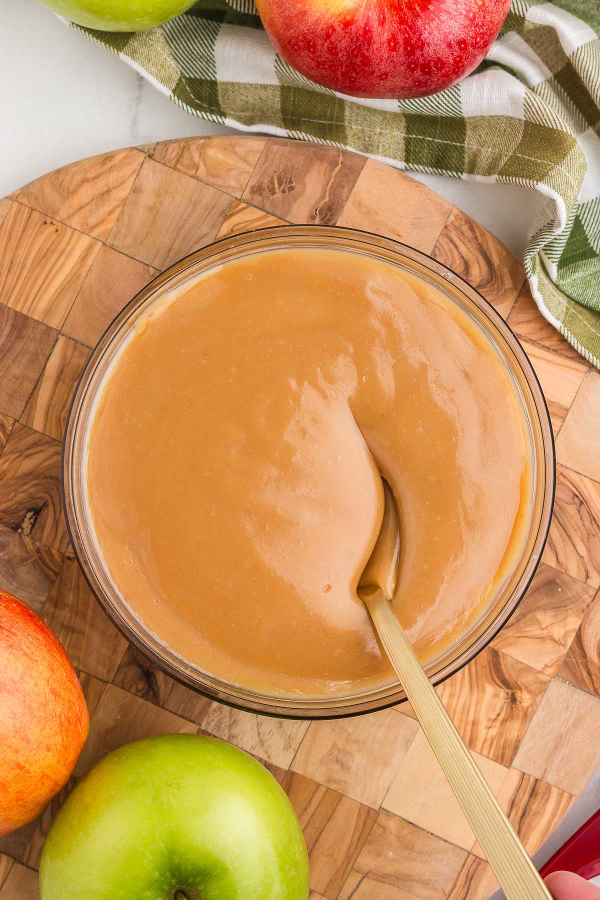 top view of caramel apple dip on a round wooden board with apples surrounding it with a spoon in the bowl