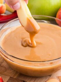 an apple being lifted out of a bowl of caramel apple dip