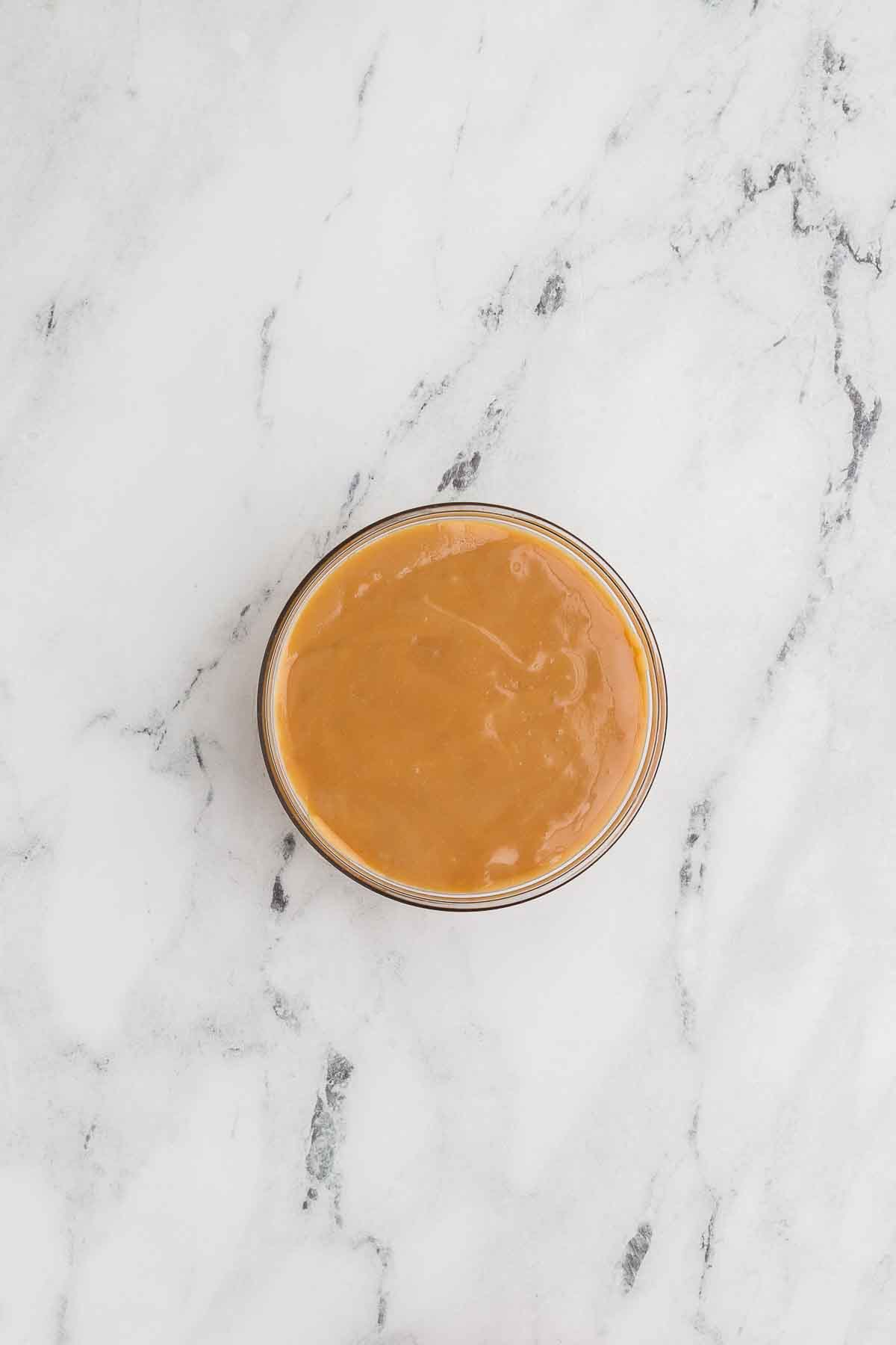 caramel apple dip in a glass bowl on a marble background