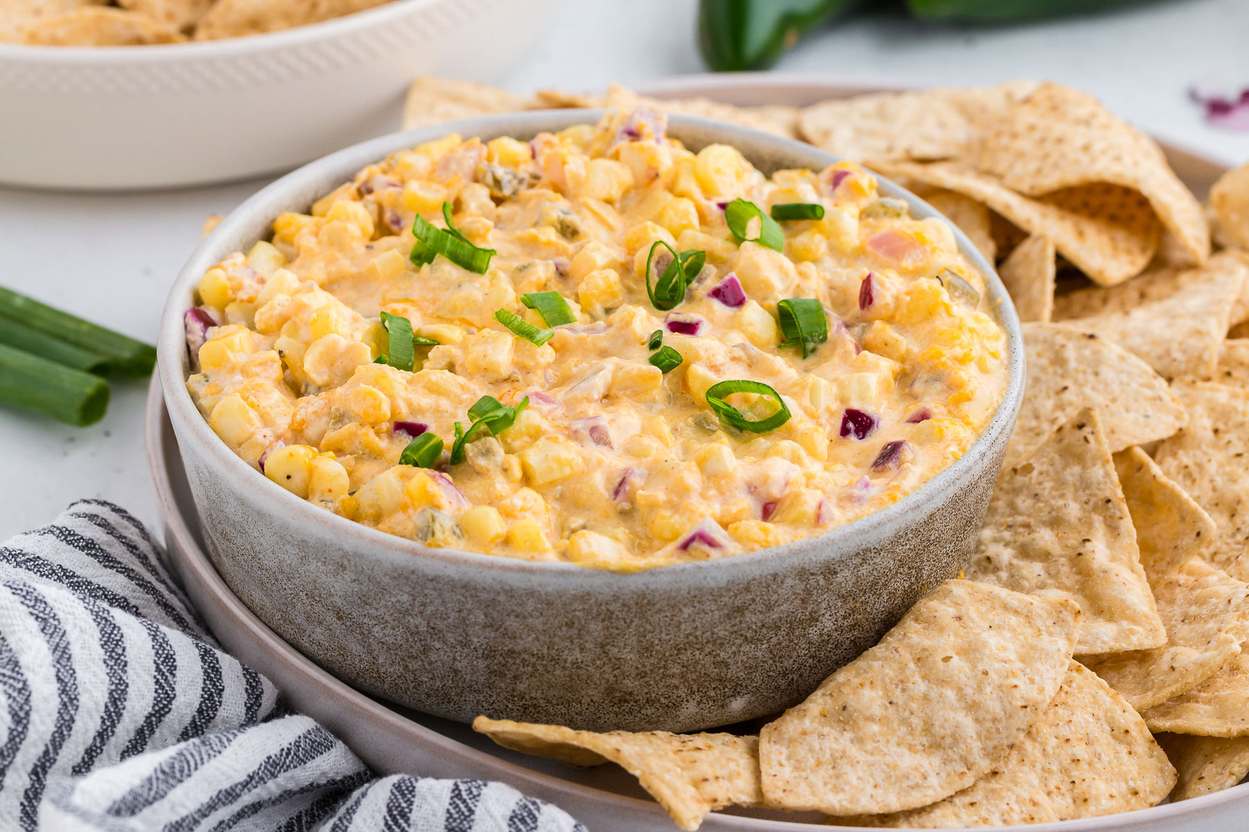 Mexican corn dip in a gray bowl with tortilla chips all around and a striped towel