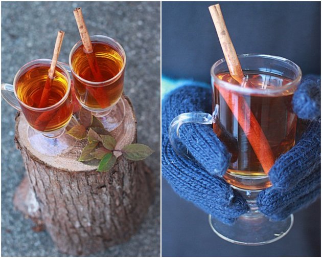 Mugs of hot spiced apple cider on a stump and mittened hands holding a warm mug of cider