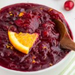 Fresh Cranberry Sauce in a white bowl with orange wedge and serving spoon