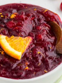 Fresh Cranberry Sauce in a white bowl with orange wedge and serving spoon