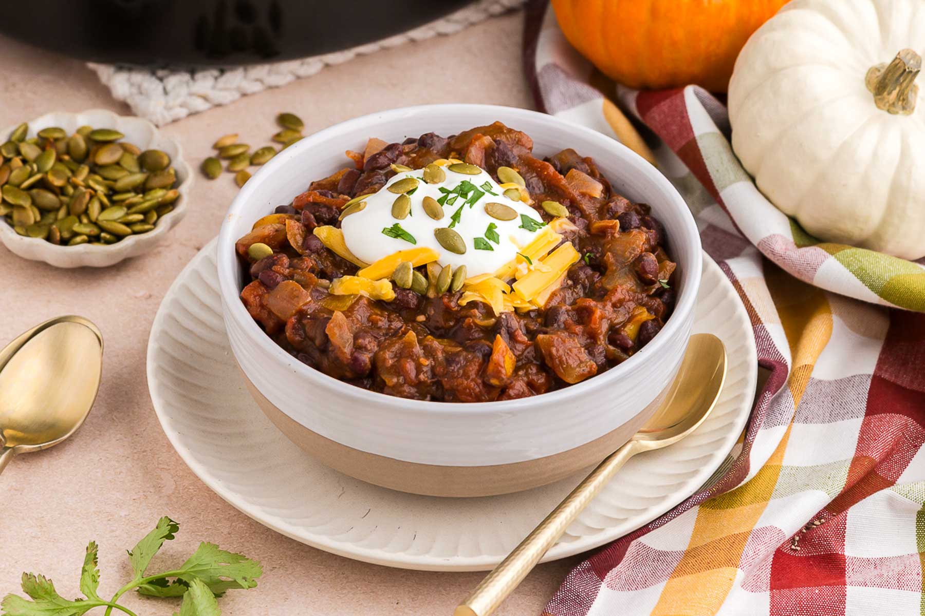 a white bowl full of pumpkin chili with mini pumpkins in the background