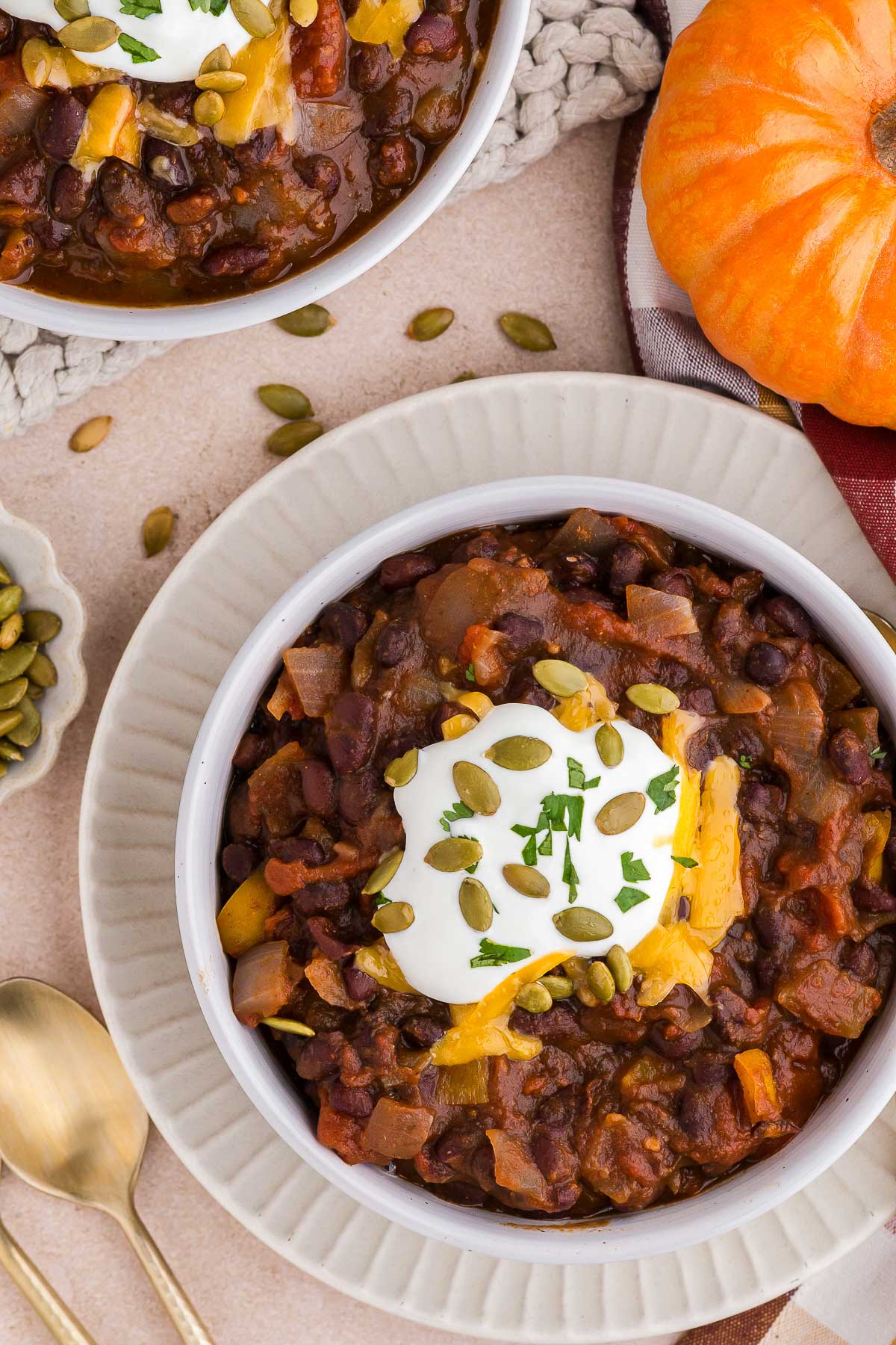 Black beans, pumpkin, and warming spices simmer together in your Crock Pot to make a meatless pumpkin chili recipe that's perfect for fall. #veganchili #vegetarianchili #pumpkinchili top view of two bowls of vegetarian pumpkin chili with assorted toppings