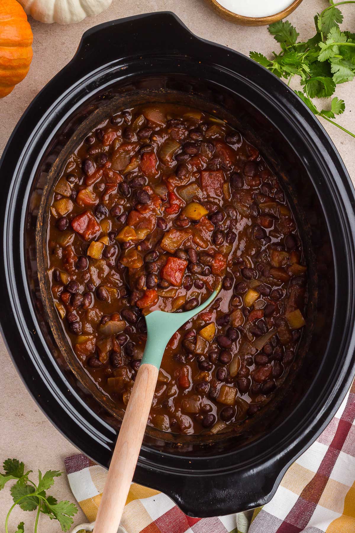 a spoon stirs freshly cooked vegetarian pumpkin chili in a black slow cooker