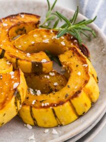 close-up of roasted delicata squash with rosemary and feta on white plates