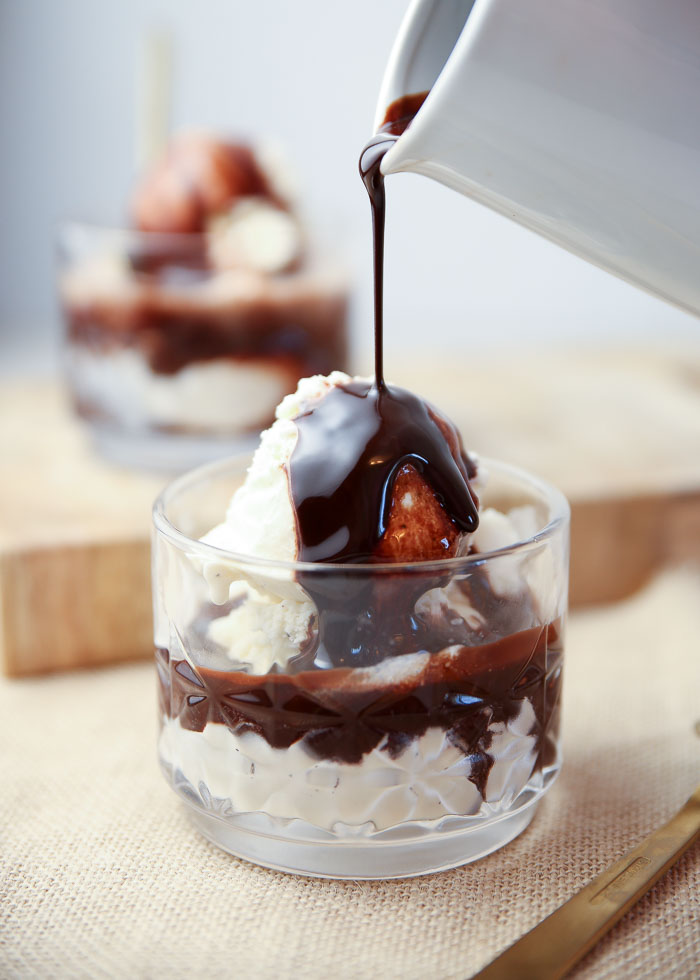 Homemade chocolate syrup being drizzled over a cup of vanilla ice cream