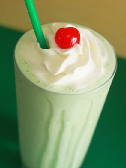 A close up of a boozy shamrock shake, a green shamrock shake cocktail, topped with whipped cream and a cherry.