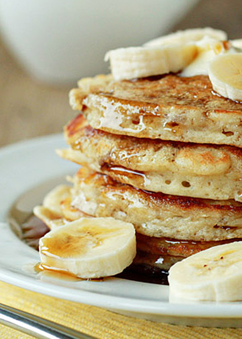 Stack of fluffy banana pancakes with pure maple syrup and banana slices