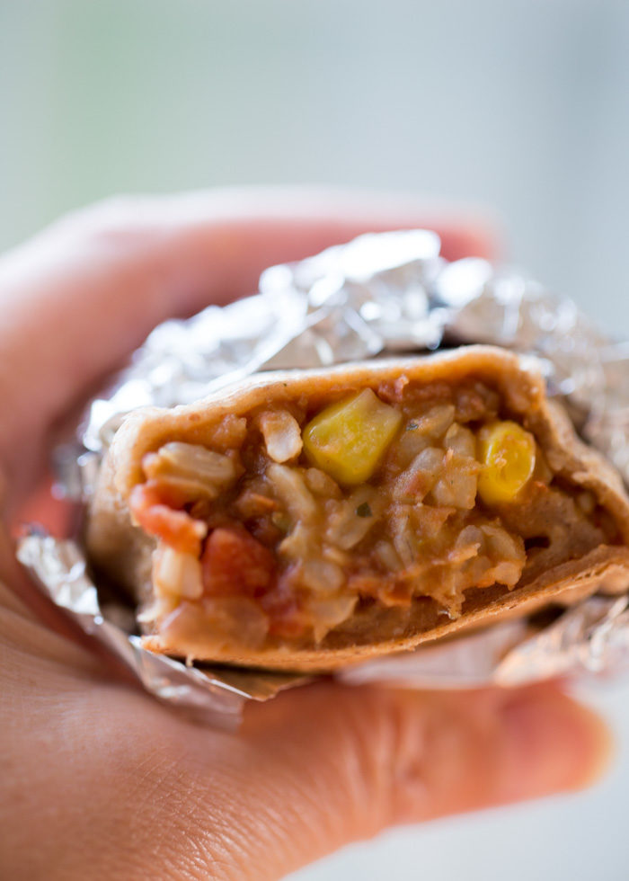 A hand holds a burrito wrapped in foil. 