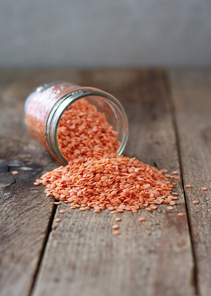 A jar of red lentils spilling onto a barn wood surface