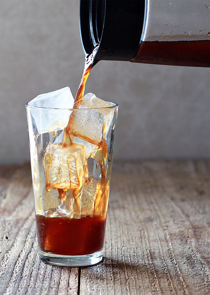 A pitcher of cold brew coffee being poured into a cup over ice. 