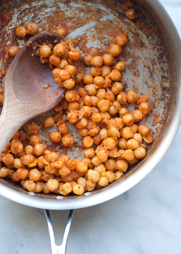 A saute pan of buffalo chickpeas with a wooden spoon on a marble countertop. 