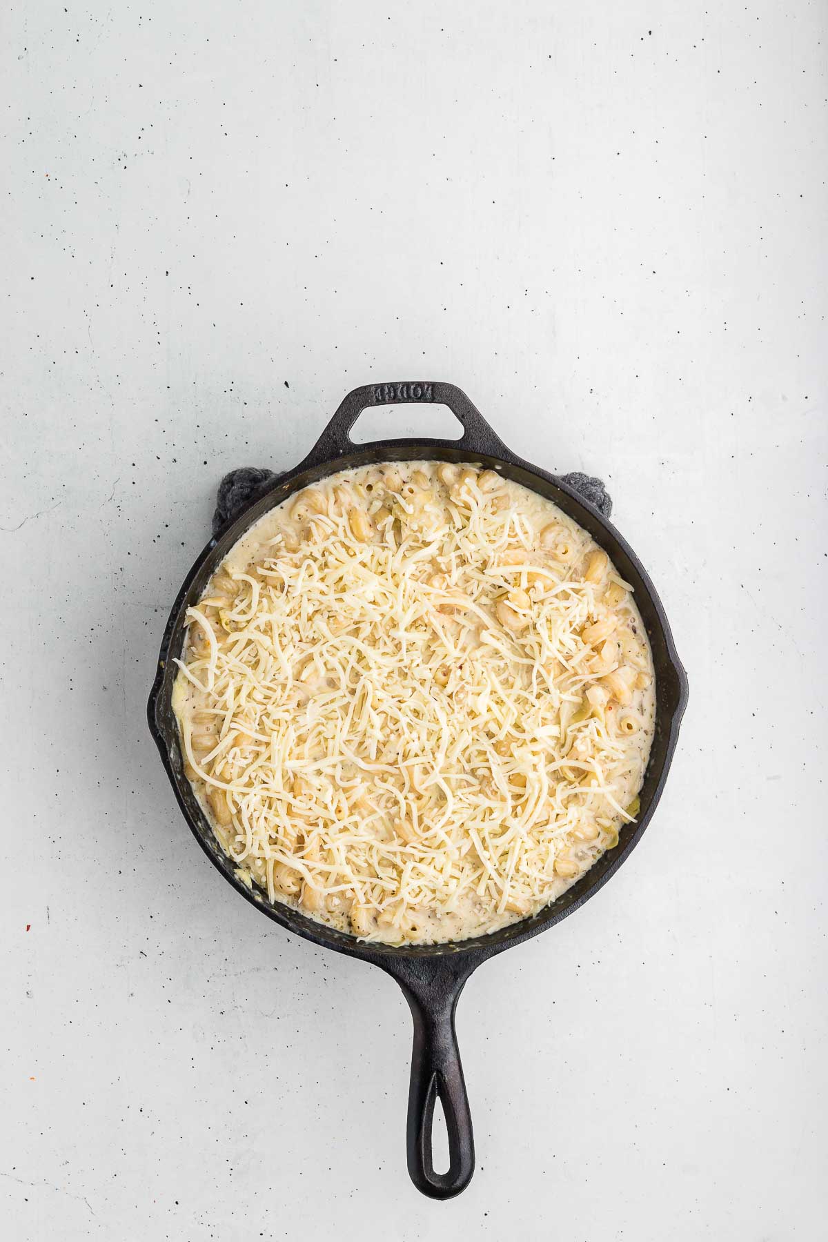 cheese added to top view of skillet with ingredients for artichoke pasta bake