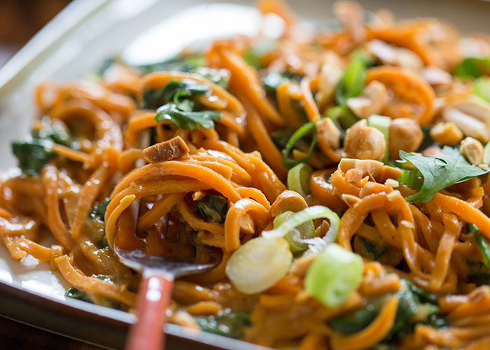 Spiralized sweet potatoes tossed with spinach, drenched in peanut sauce, and topped with crunchy peanuts. Increase the protein factor by topping with baked tofu or - if any carnivores are at your table - some grilled chicken. #vegan #onedishtwoways #sweetpotatonoodles