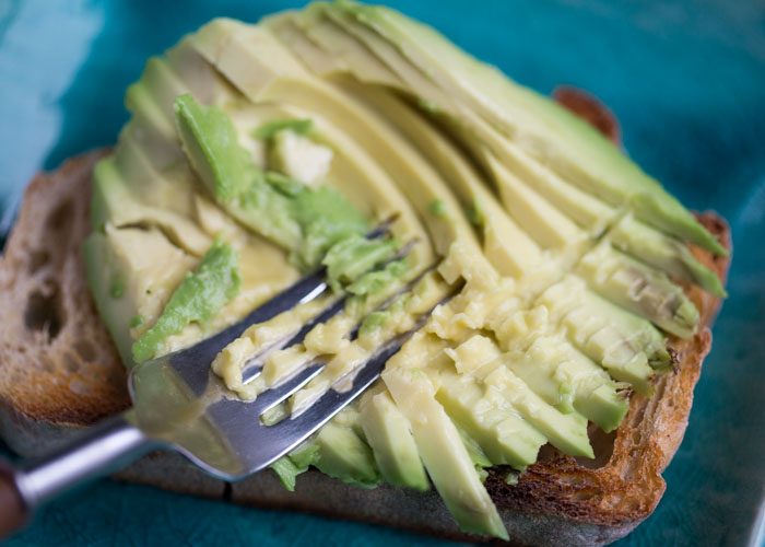 Mushing the avocado on a piece of toast. 