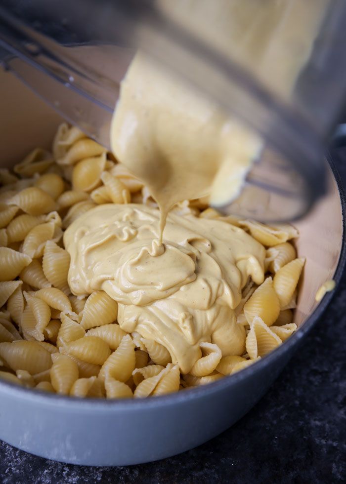 Creamy dairy free mac and cheese sauce is being poured into a pot of cooked pasta.