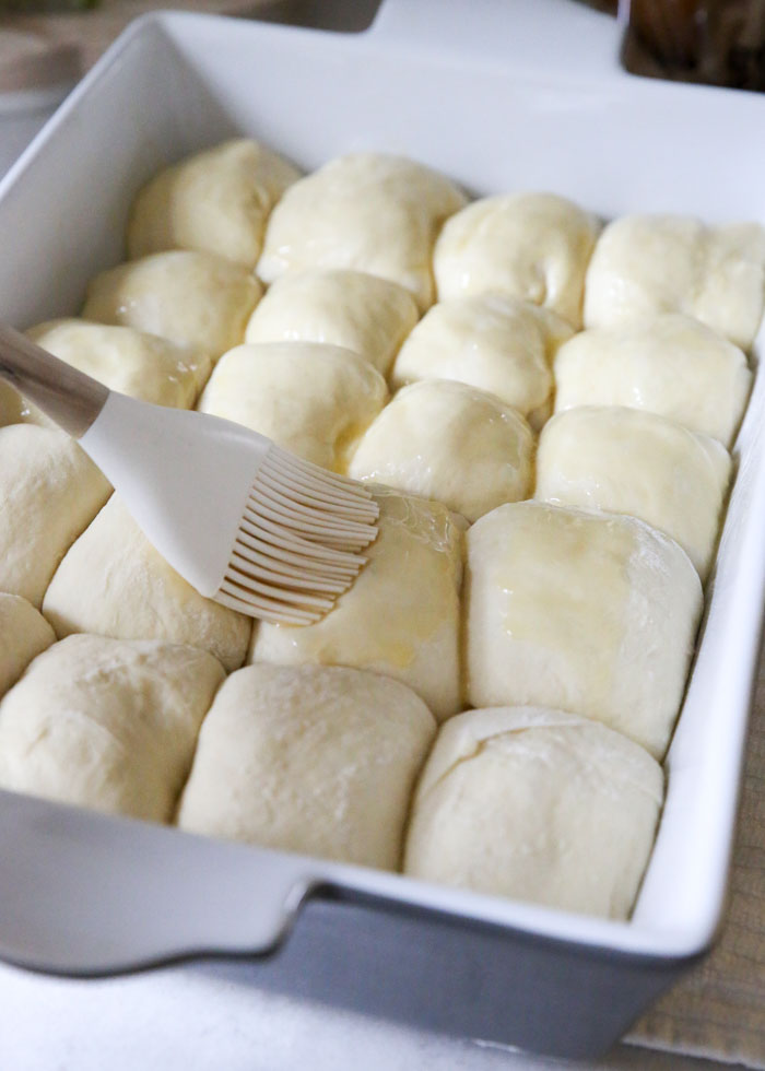 Brushing butter on the tops of soft and fluffy vegan dinner roll dough