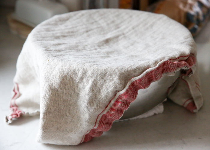 A bowl of dough rising on the counter, covered by a kitchen towel