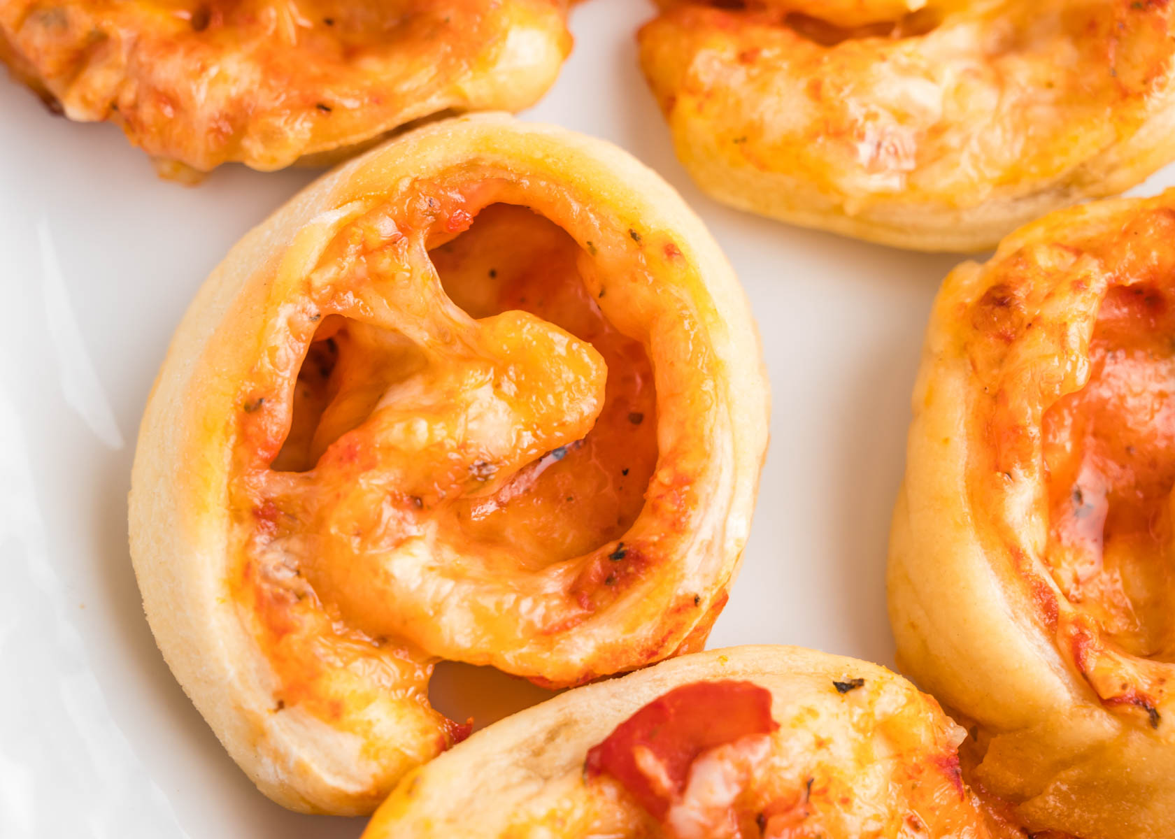 A white platter with pizza pinwheels ready to serve