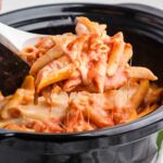 Crock Pot Baked Ziti in a black Crock Pot with a white serving spoon lifting out a portion