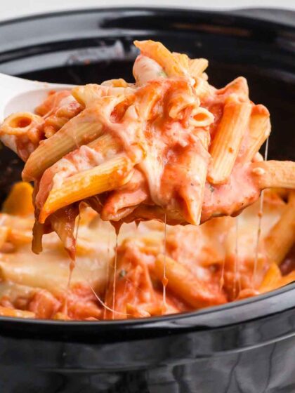 Crock Pot Baked Ziti in a black Crock Pot with a white serving spoon lifting out a portion