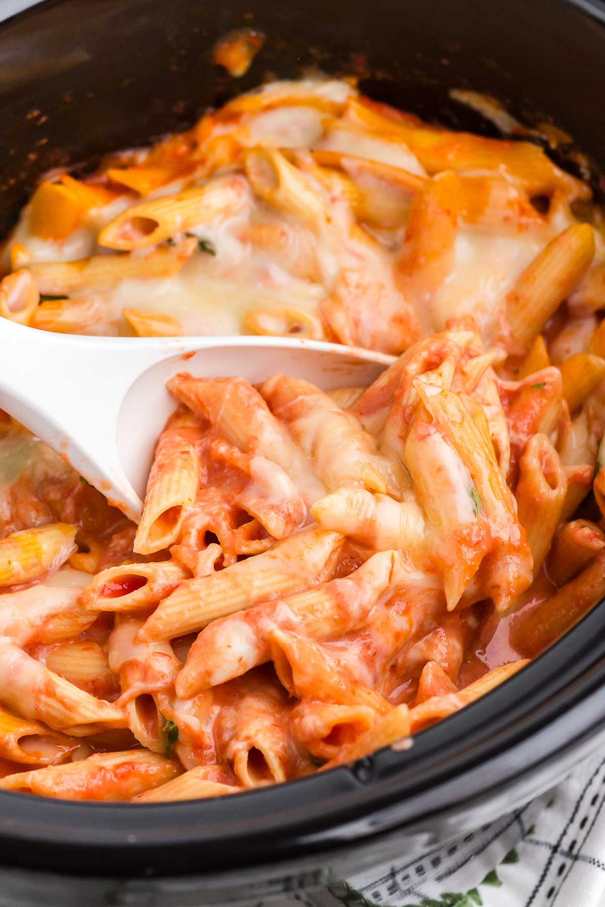 Crock Pot Baked Ziti in a black Crock Pot being scooped out with a white spoon