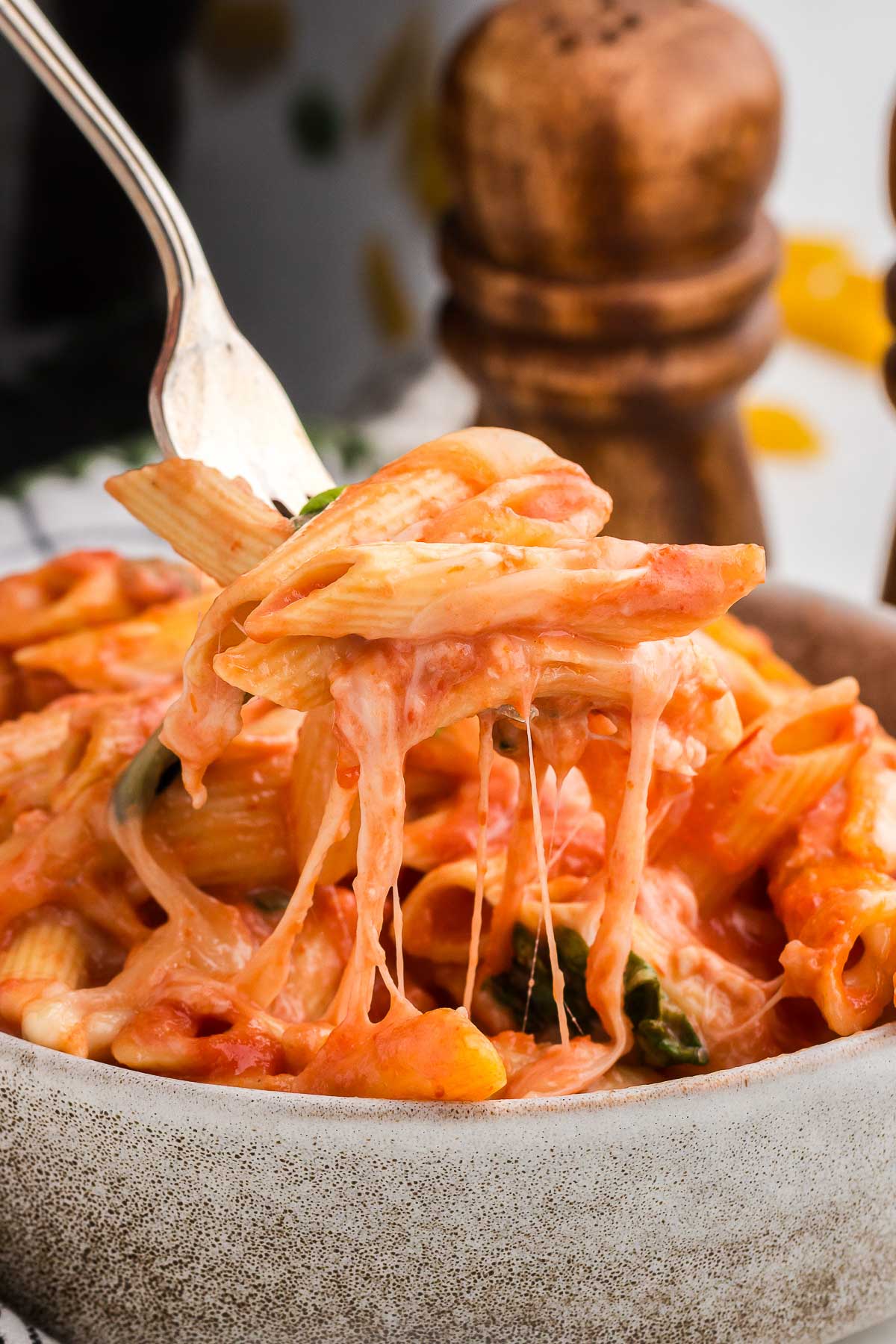 A bites of Crock Pot Baked Ziti is lifted out of a rustic bowl with a silver fork.