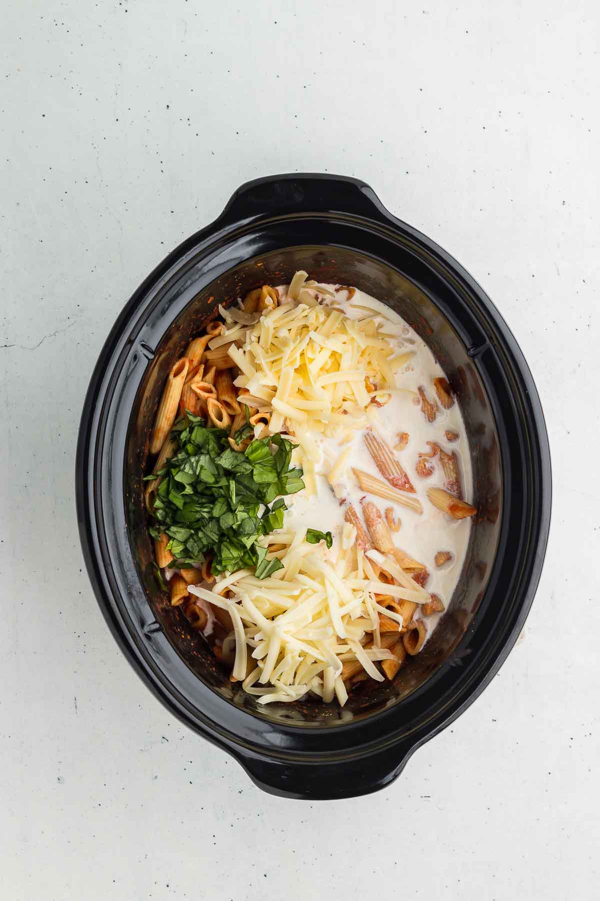 Stirring heavy whipping cream, cheeses, and basil into Crock Pot Baked Ziti