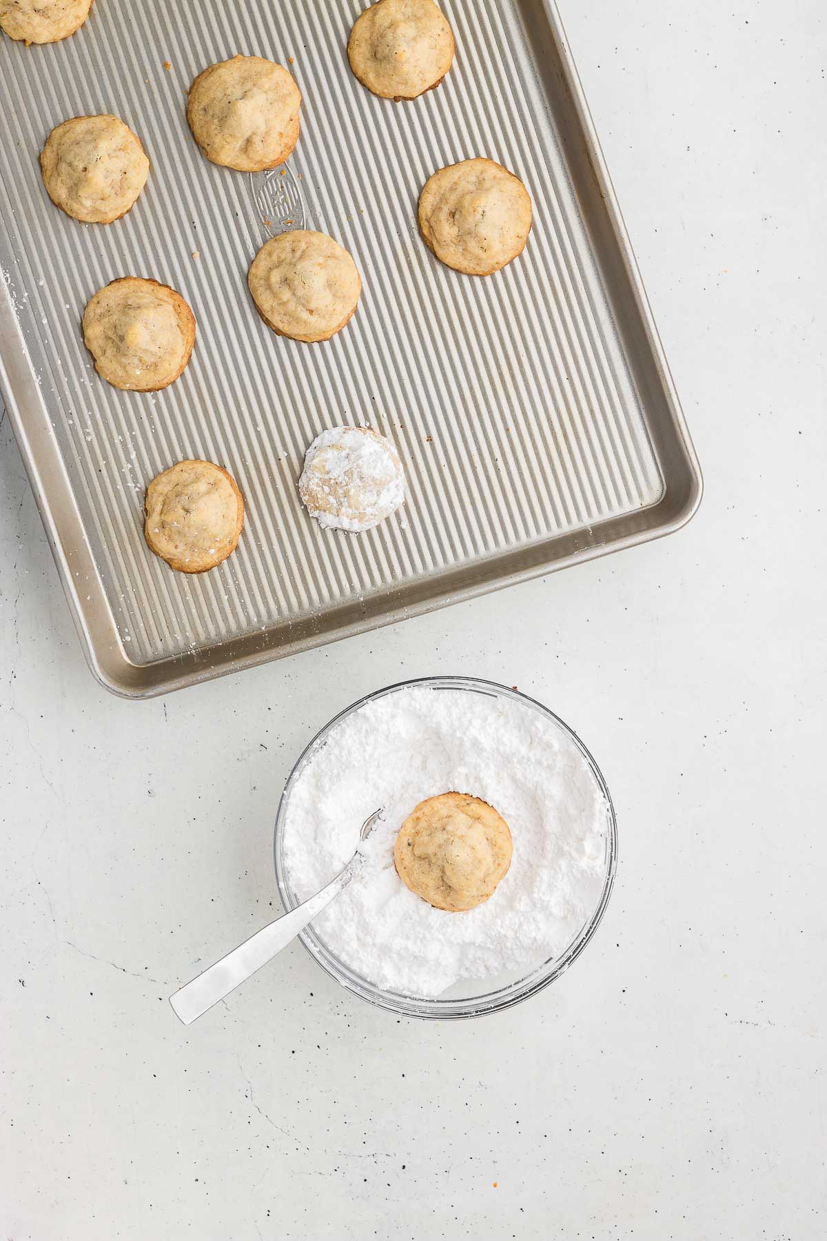 Baked hidden kiss cookies being tossed in powdered sugar