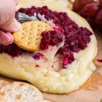 a cracker scooping melty brie and cranberry sauce
