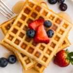 a top view of a stack of three waffles with syrup and berries