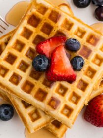 a top view of a stack of three waffles with syrup and berries