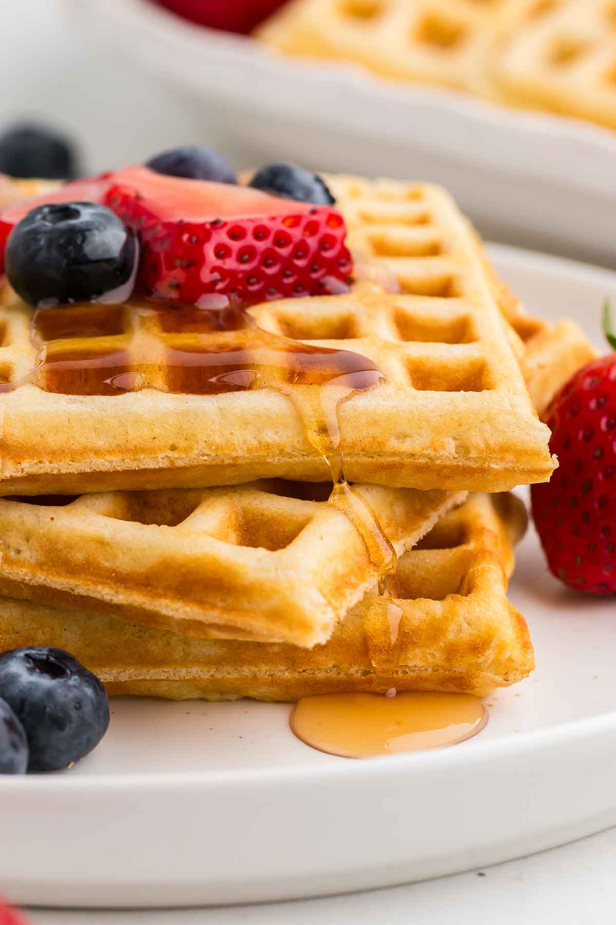 A stack of homemade waffles with berries and syrup on a white plate