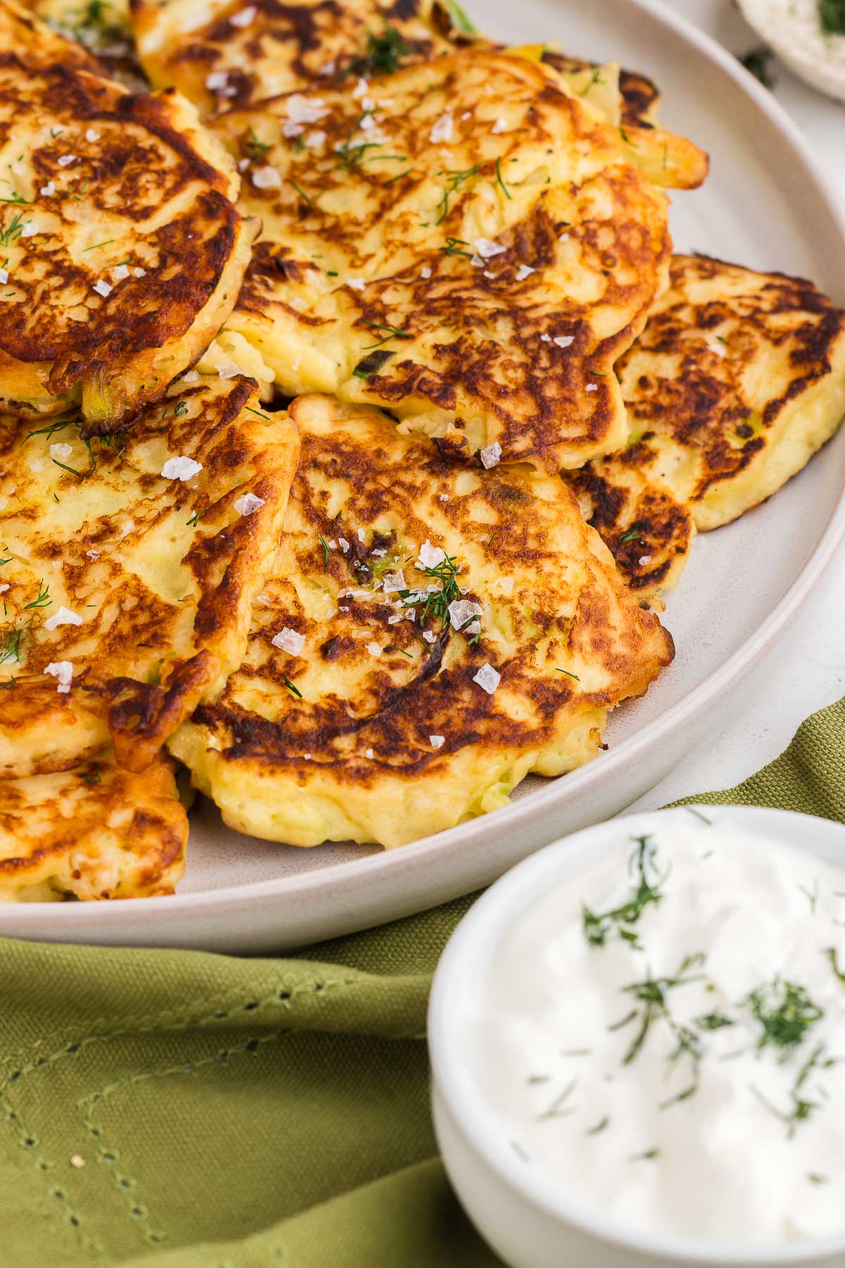 pile of golden colcannon cakes on a white plate with flaky sea salt and fresh dill
