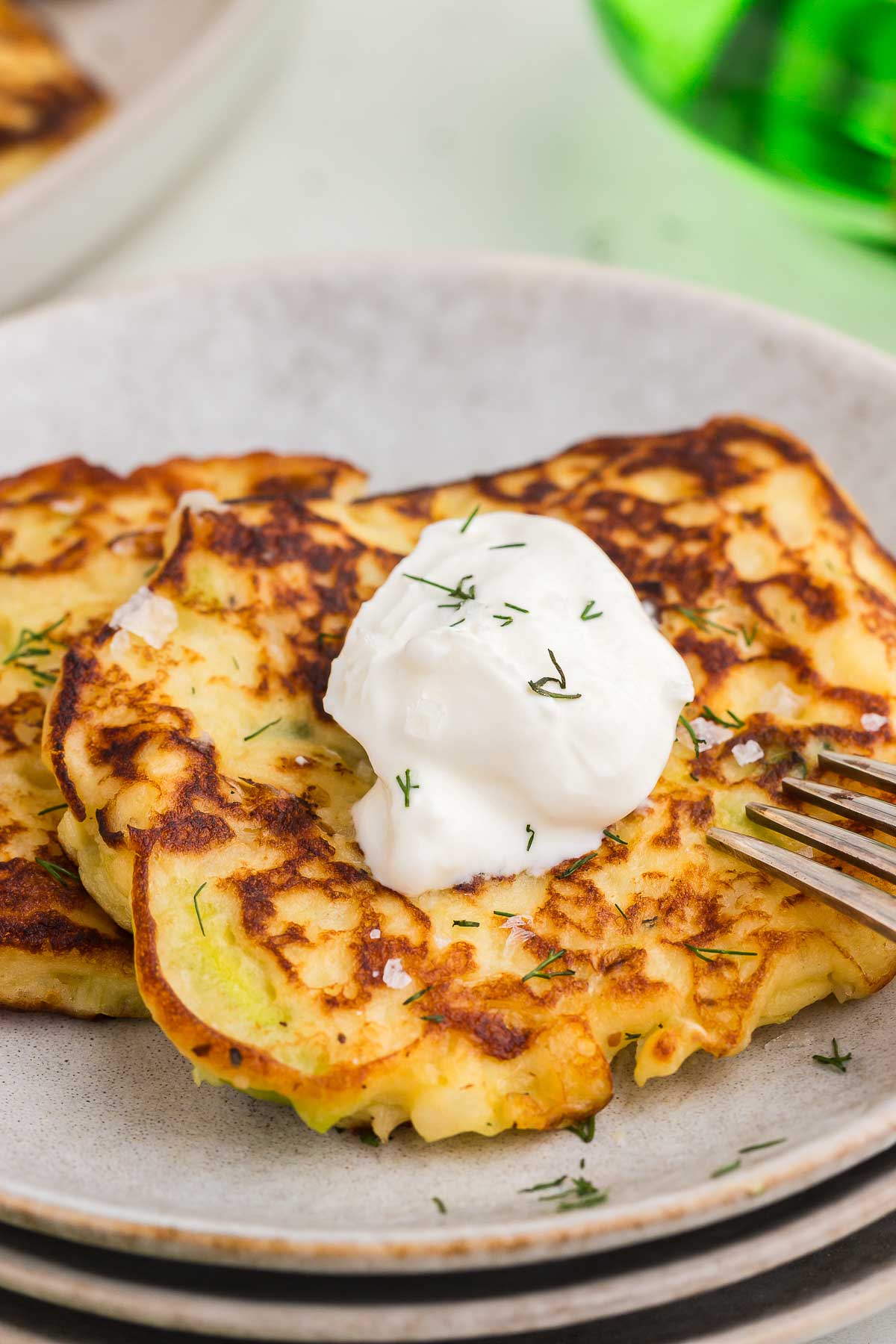 colcannon cakes on a stack of gray stoneware plates with sour cream and a silver fork