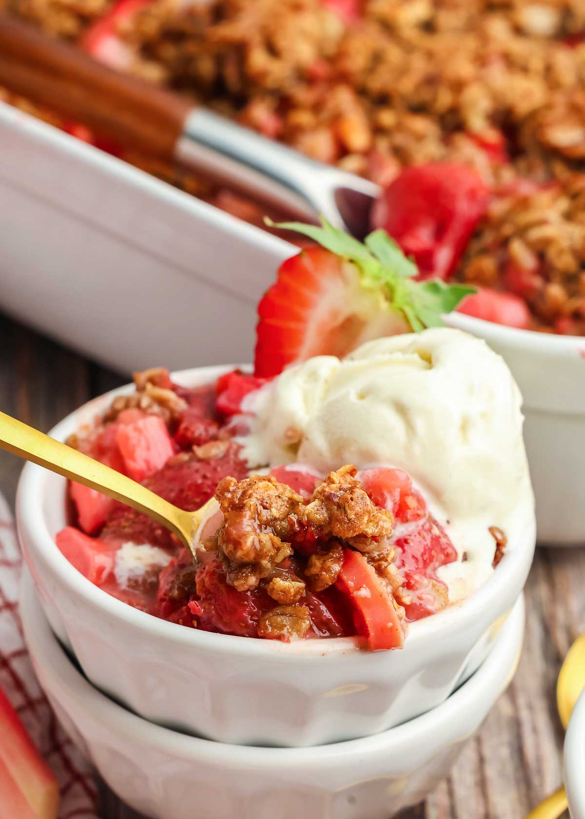 bowl full of Strawberry Rhubarb Crisp with a gold spoon in it and vanilla ice cream