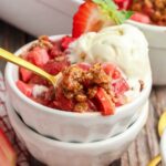 bowl full of Strawberry Rhubarb Crisp with a gold spoon in it and vanilla ice cream
