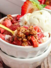 bowl full of Strawberry Rhubarb Crisp with a gold spoon in it and vanilla ice cream