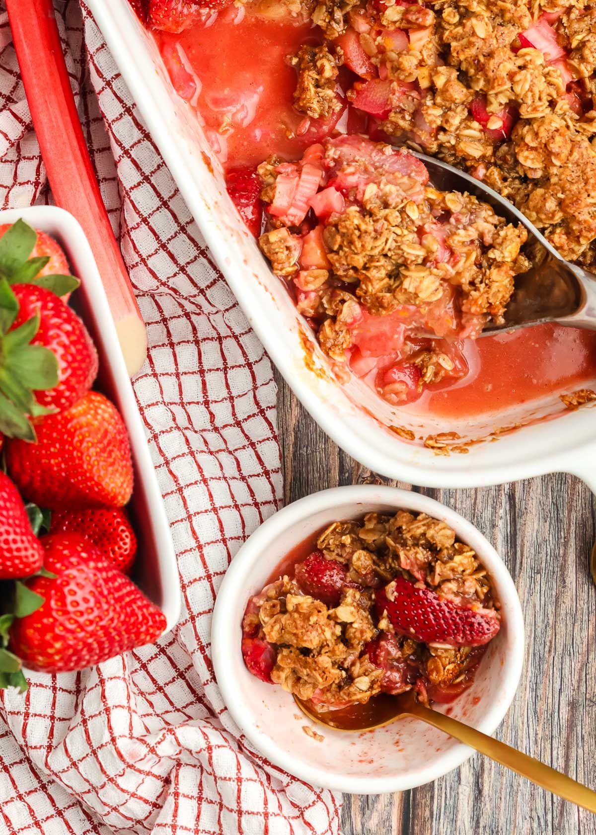 white bowl full of Strawberry Rhubarb Crisp alongside a 9x13 pan of Strawberry Rhubarb Crisp and strawberries on the side. 