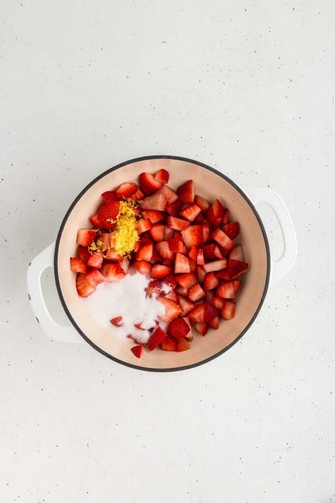 ingredients for strawberry sauce in a white cast-iron pan.