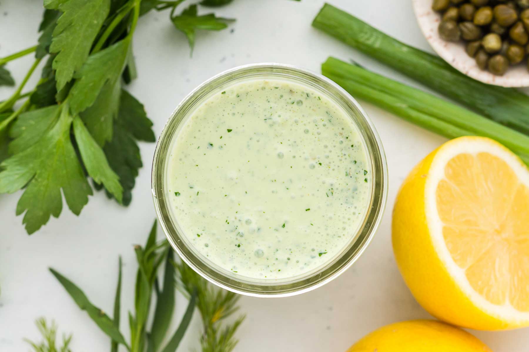 Green Goddess Dressing in a mason jar with ingredients all around it