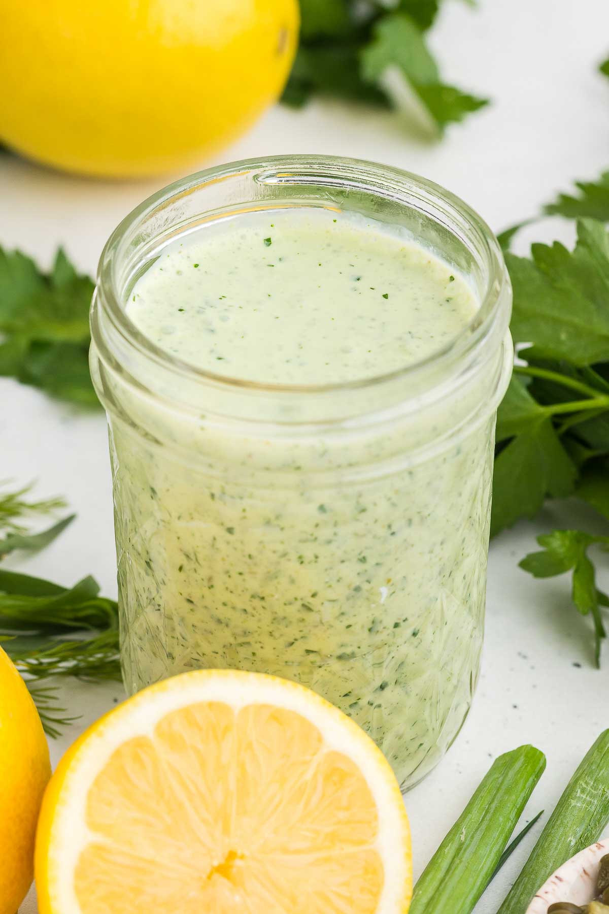 Green Goddess Dressing in a jar with lemon, scallions, and herbs in the background