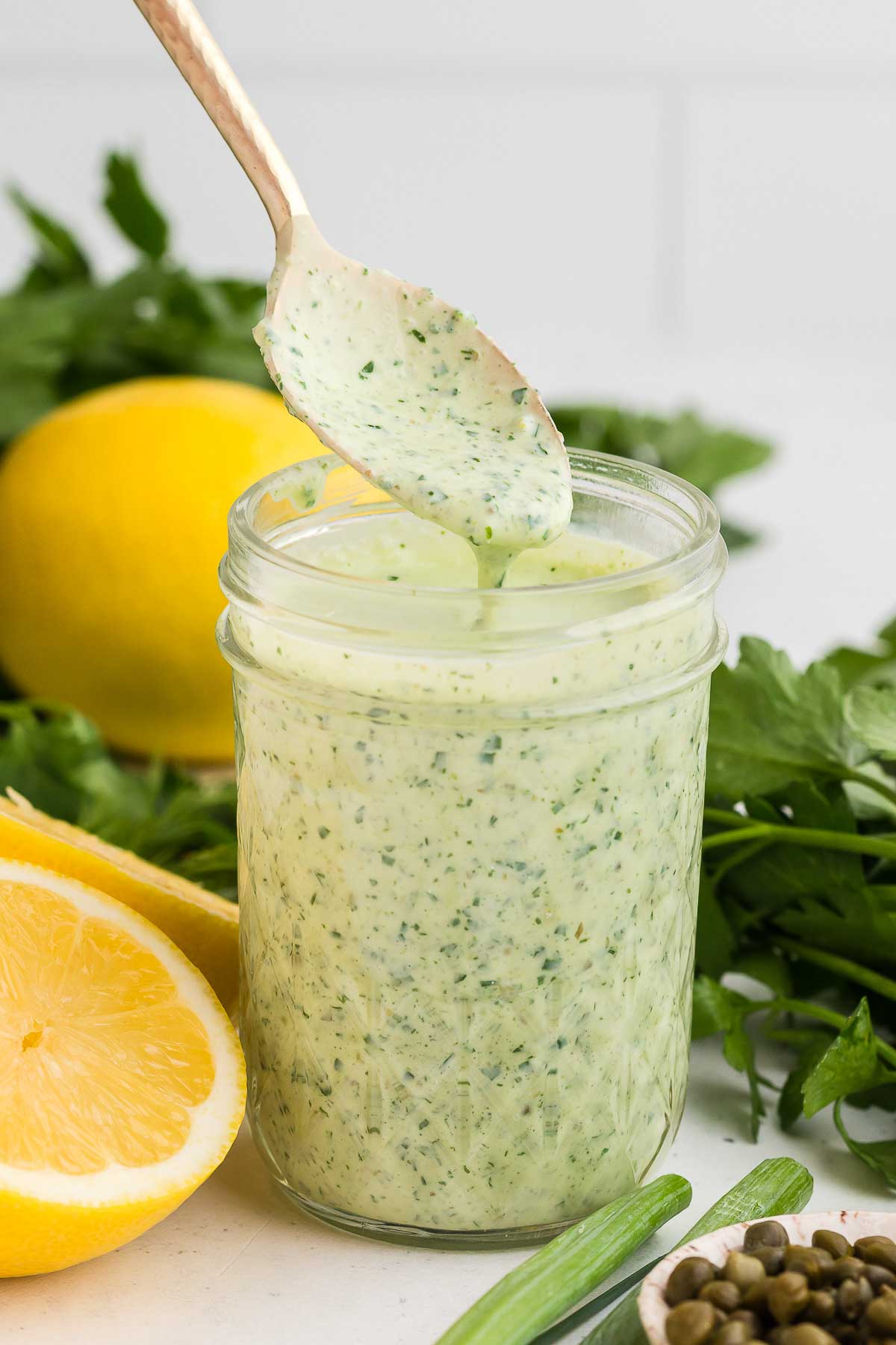 Green Goddess Dressing in a jar with a spoon lifting some dressing out of the jar