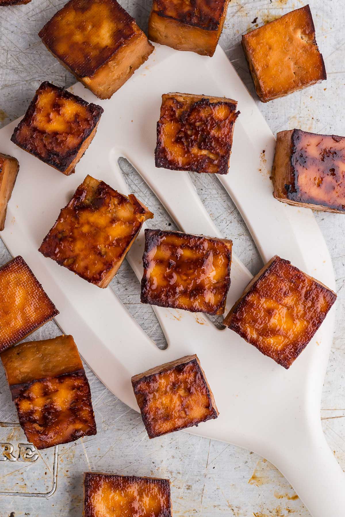 close up of marinated baked tofu being scooped up with a spatula