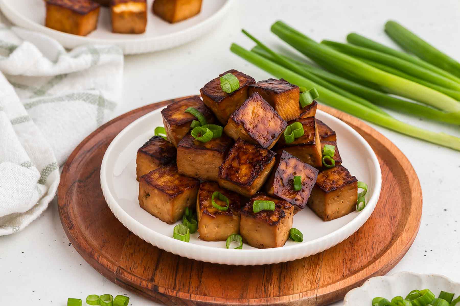 Baked tofu on a plate with scallions in the background