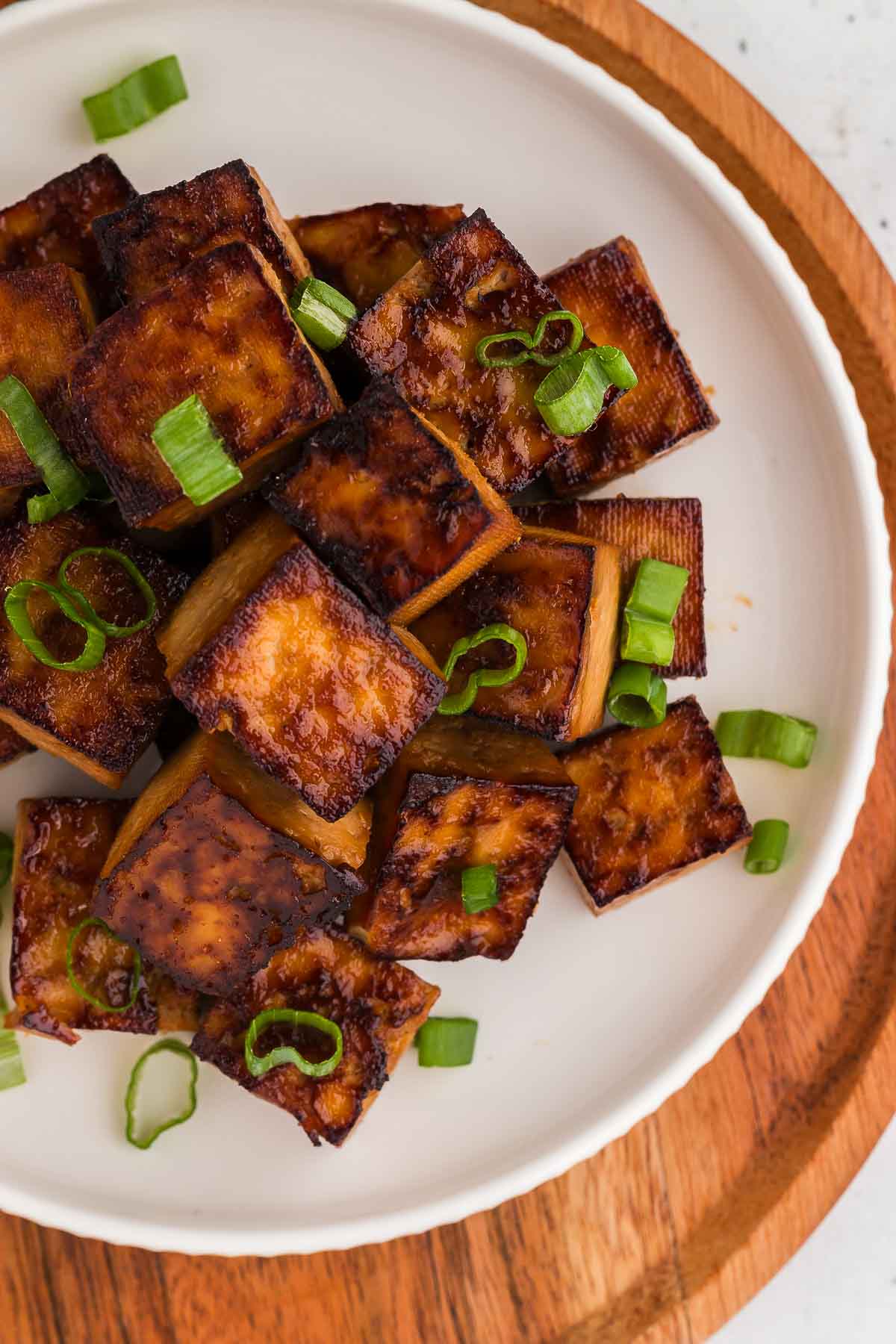 Baked tofu on a white plate and wooden charger