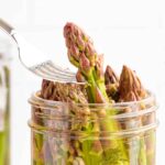 A fork lifts a stalk of pickled asparagus out of a jar of Quick Pickled Asparagus